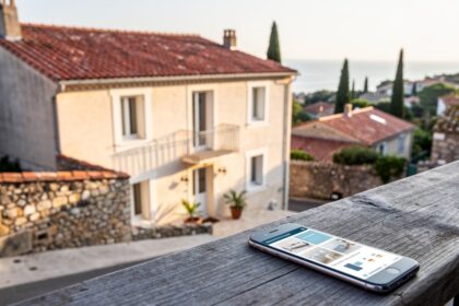 Maison de location de vacances en bord de Méditerranée et smartphone affichant une annonce sur une table en bois au premier plan.