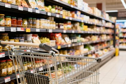 Rayon de supermarché aux étagères remplies de produits alimentaires, avec un chariot métallique vide au premier plan.