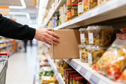 Rayon de supermarché garni de produits alimentaires emballés, une main attrapant une boîte en carton.