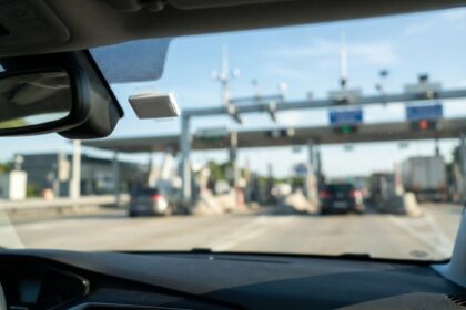 Badge de télépéage blanc fixé derrière le pare-brise d'une voiture approchant une gare de péage d'autoroute