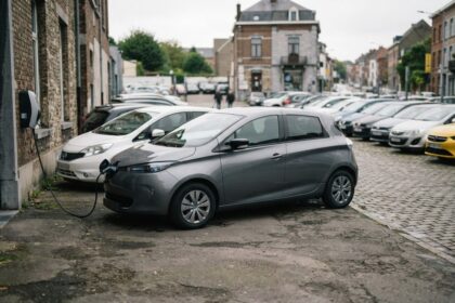 Petite voiture électrique grise en charge le long d'une rue pavée bordée de voitures d'occasion
