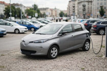 Voiture électrique compacte grise en charge sur un parking de voitures d'occasion, câble branché sur la prise latérale.